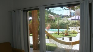A room with a sliding glass door leading to a patio with a hammock, potted plants, and a pool. - Pousada Don Pablo (Bombinhas)