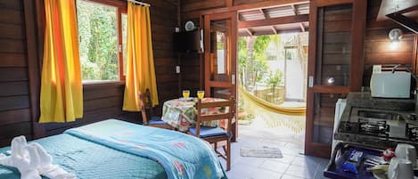 A cozy room with a bed, a small table with chairs, a kitchen area, and a view of the outdoors.