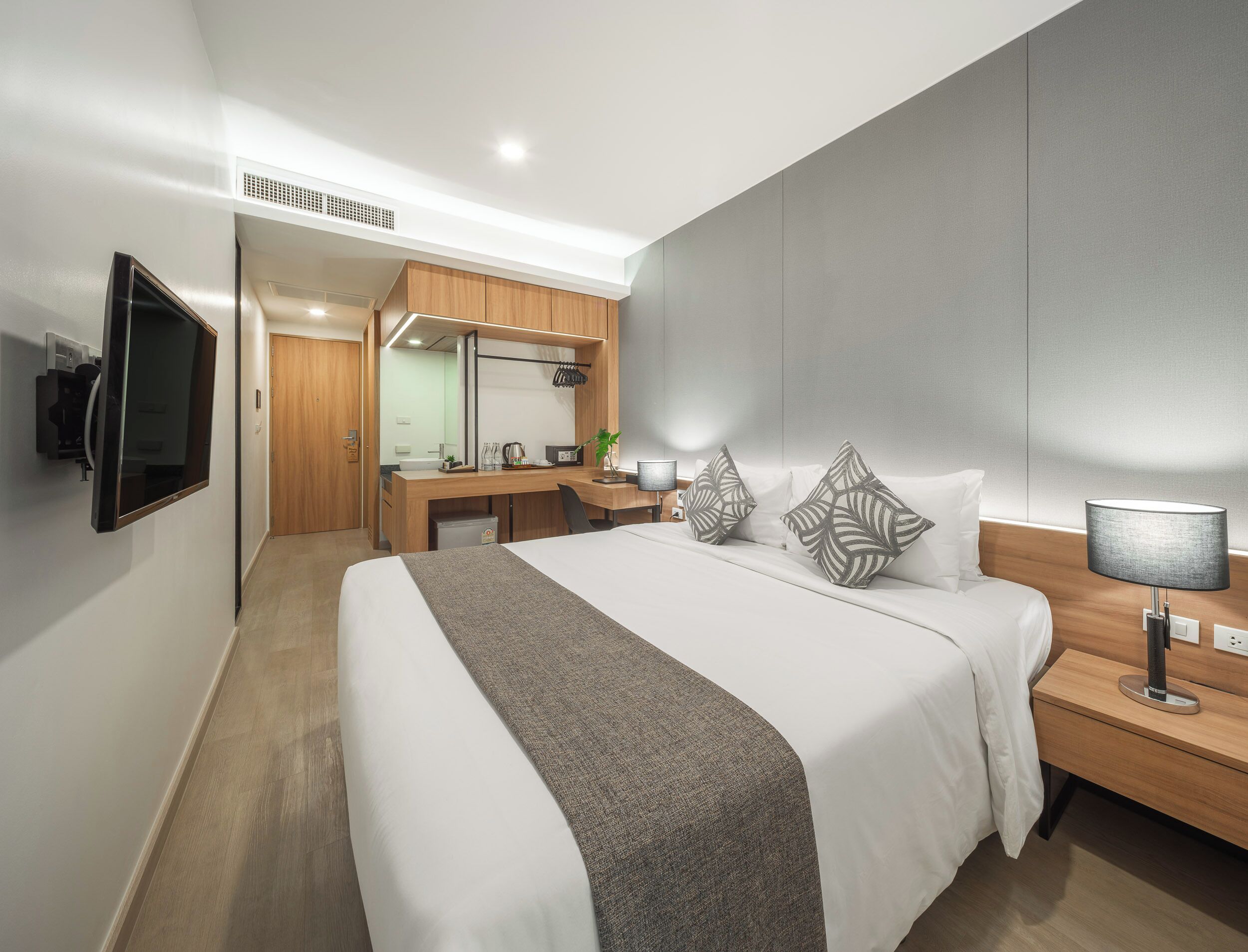 A hotel room with a bed, bedside table, lamp, TV, desk, and a mirror.