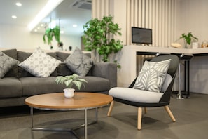 A modern living room with a grey sofa, a round wooden coffee table, and a black and grey armchair. There are patterned pillows on the sofa and a potted plant on the table. - Nap in Chiangmai (Chiang Mai)