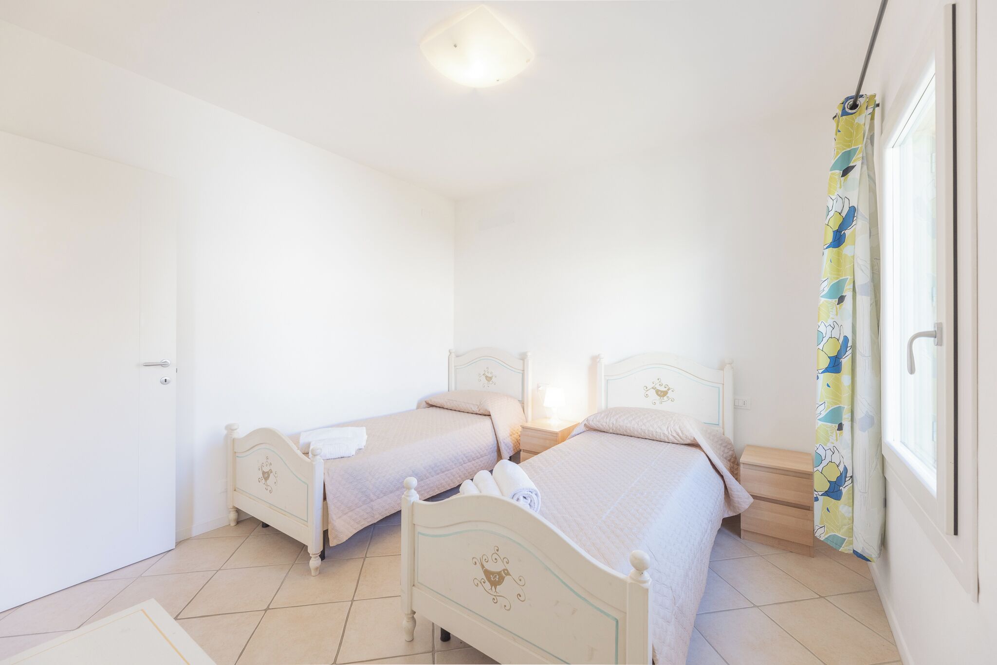 Un dormitorio con dos camas, una mesita de noche, una ventana con cortina y una puerta.
