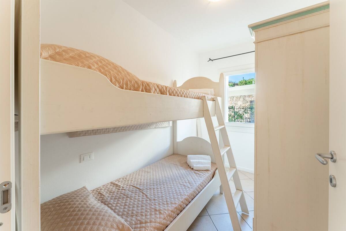 Une chambre avec un lit superposé, une échelle, une porte et une vue sur l’extérieur.