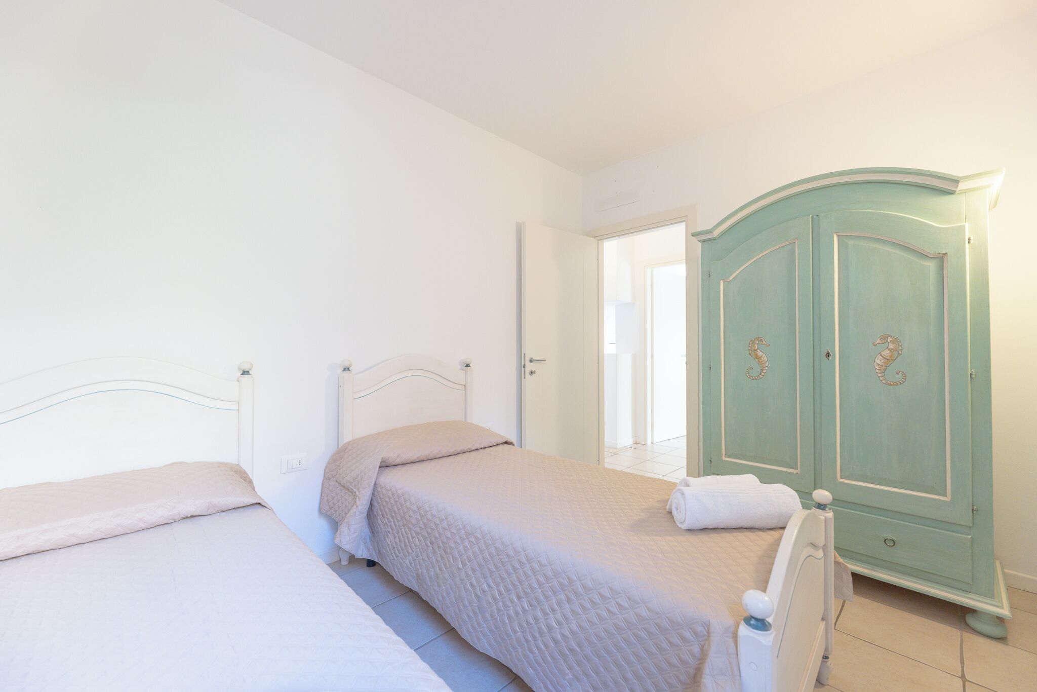 A bedroom with two beds, a wardrobe, and a door leading to another room.