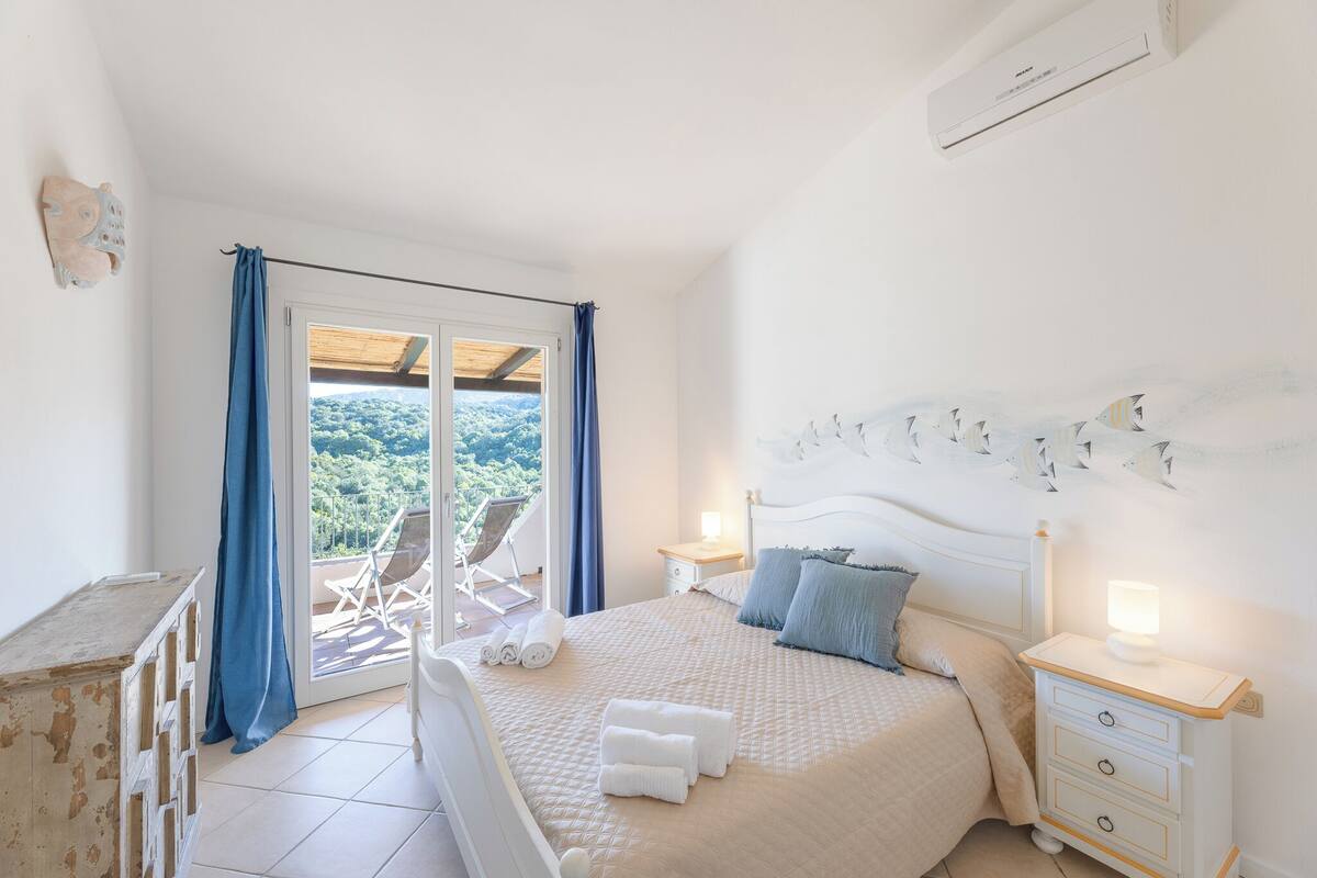 Une chambre à coucher comprenant un lit, des tables de chevet, une commode et donnant sur l’extérieur.