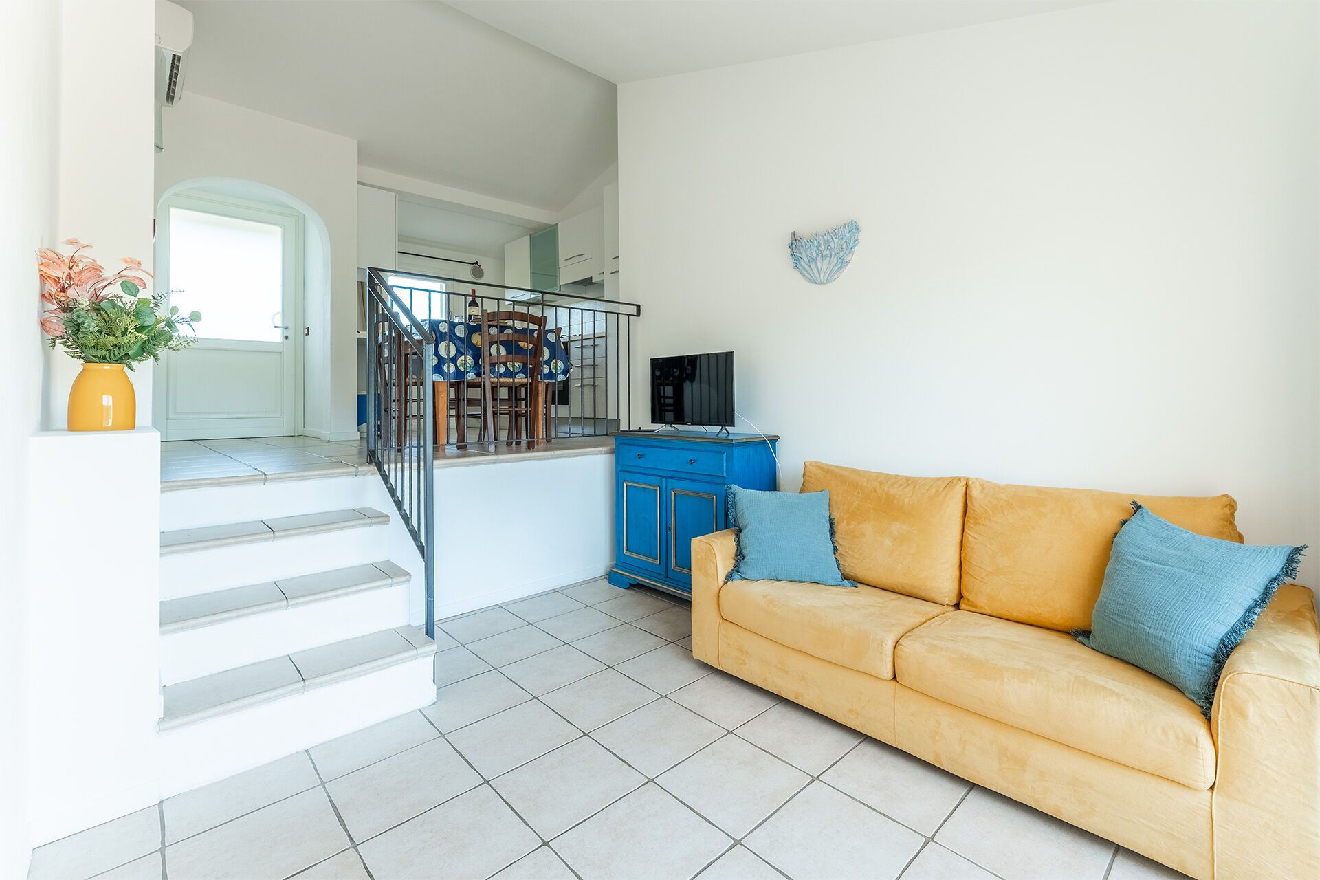 Una sala de estar con un sofá, un mueble azul y una escalera que lleva a otra habitación.