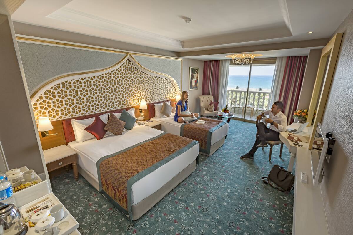 Habitación de hotel con dos camas, un escritorio y una silla. Se ve el océano a través de ventanas amplias.
