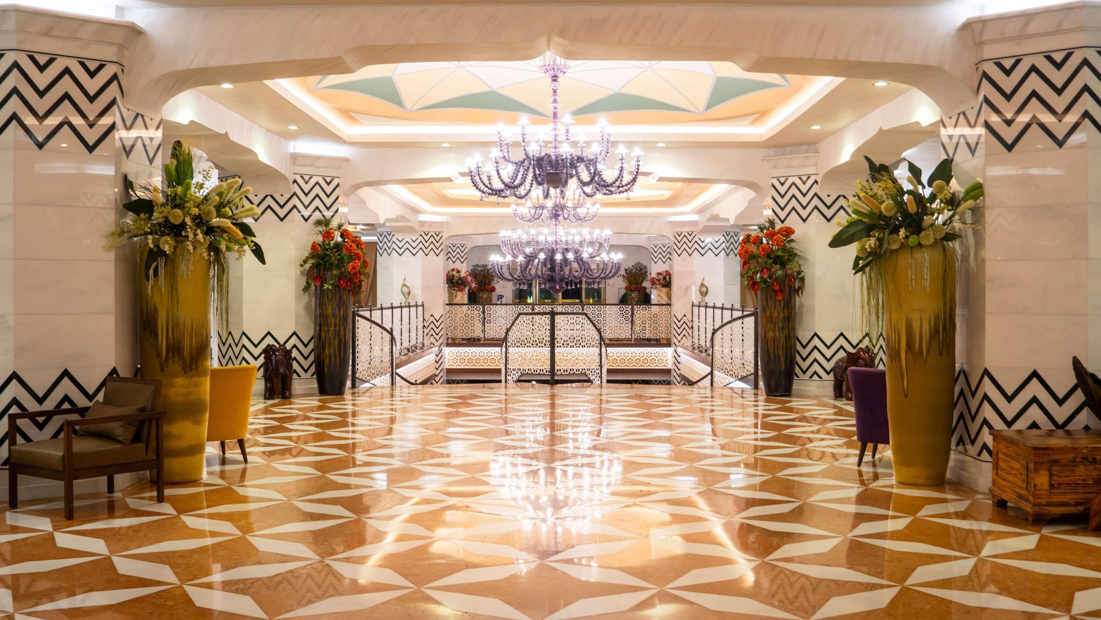 A lobby with a geometric patterned floor, a central staircase, and a chandelier.