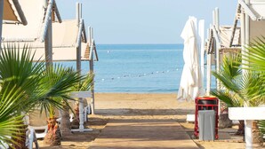 Un sentier en bois mène aux parasols et aux chaises longues de la plage, offrant une vue dégagée sur l’océan.