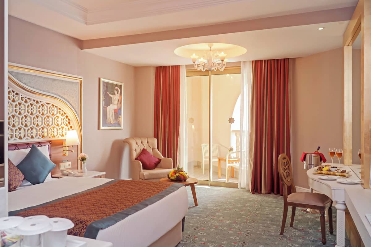 Habitación de hotel con una cama grande, un espacio de descanso con una silla y una mesa, un escritorio con silla, y un comedor con una mesa dispuesta para dos.