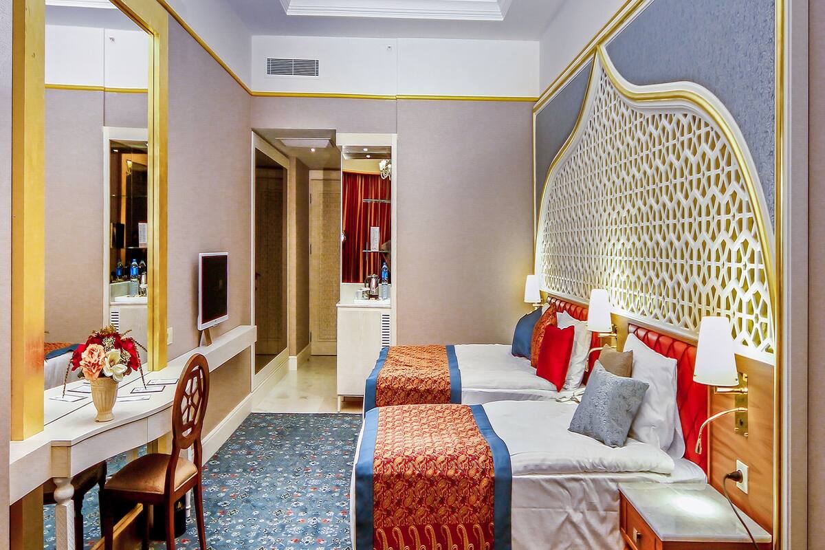 Habitación de hotel con dos camas, un escritorio, una silla, un televisor y una zona de comedor con fruteros y vasos.