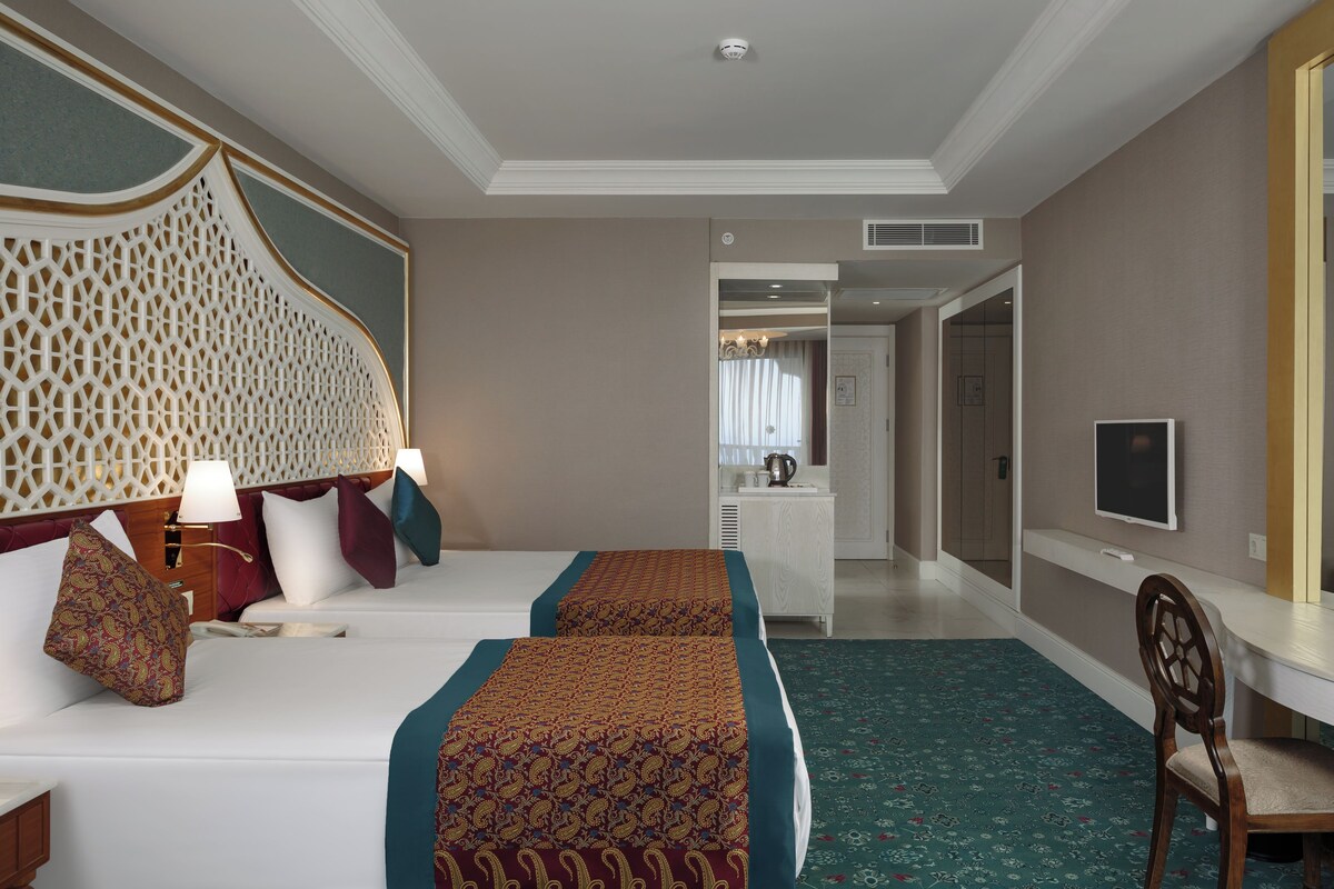 A hotel room with two beds, a desk, a chair, a TV, and a bathroom visible through an open door.