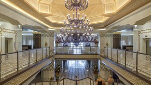 Un vaste hall d’entrée agrémenté d’un grand lustre, de plusieurs étages et de balustrades aux motifs complexes.