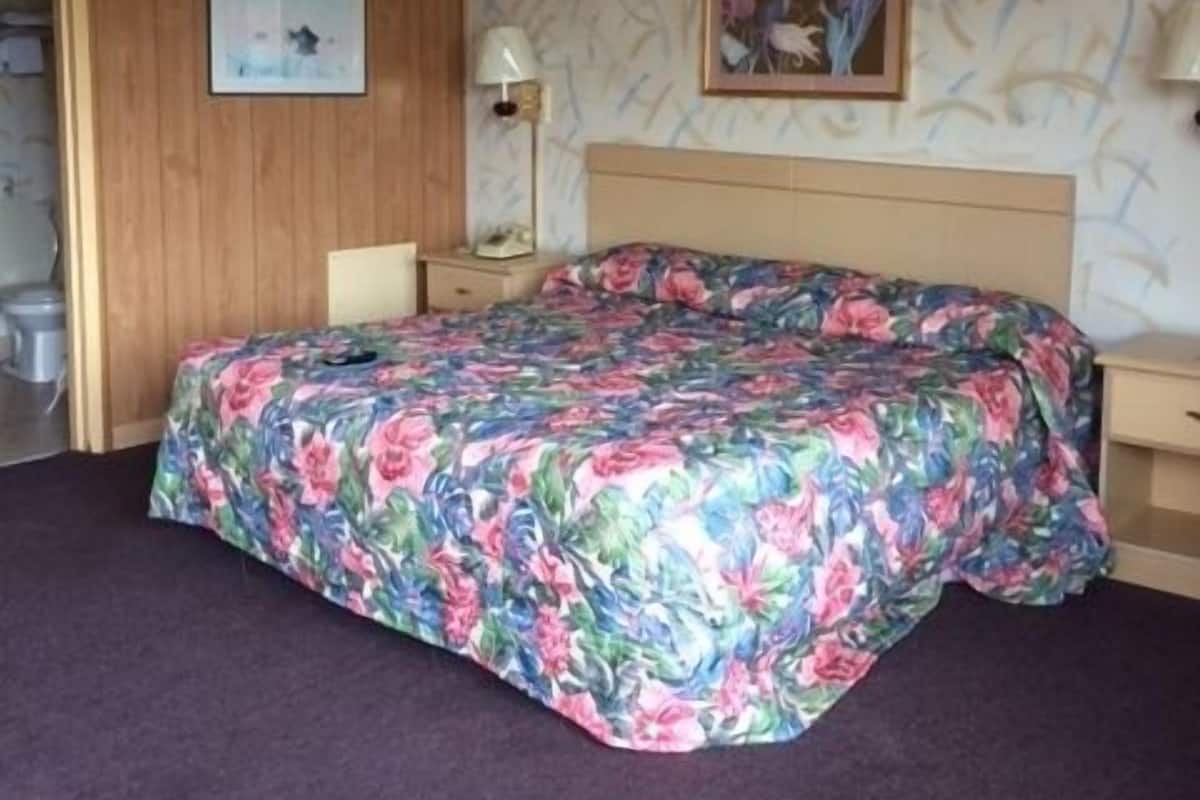 A room with a bed, a nightstand, a lamp, and a painting on the wall.