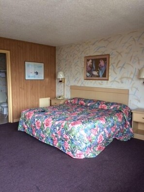 A room with a bed, a nightstand, a lamp, and a painting on the wall.