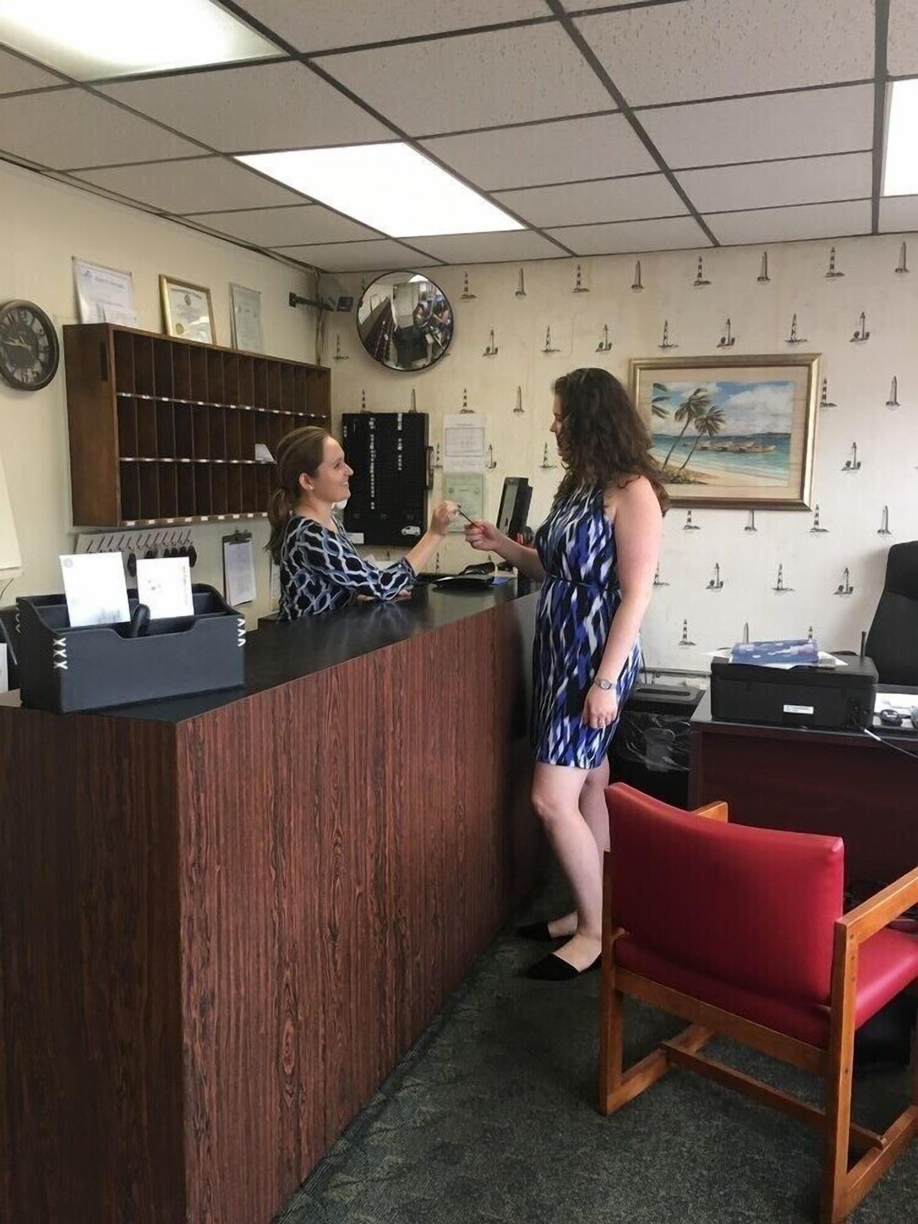 A reception area with a wooden reception desk, a red chair, a clock, framed certificates, and a wall with nautical-themed decorations.