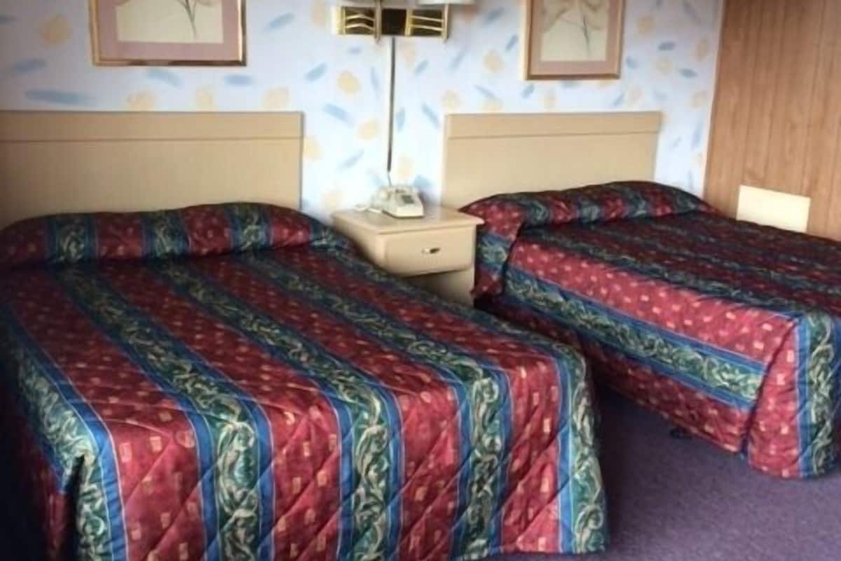A room with two beds, each with a patterned bedspread, a bedside table with a lamp, and two framed pictures on the wall.