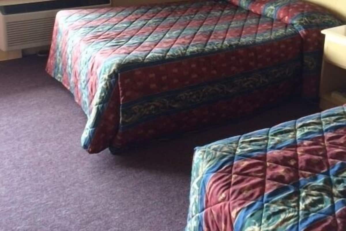 A room with two beds, a window with curtains, a radiator, and a wall with a framed picture.