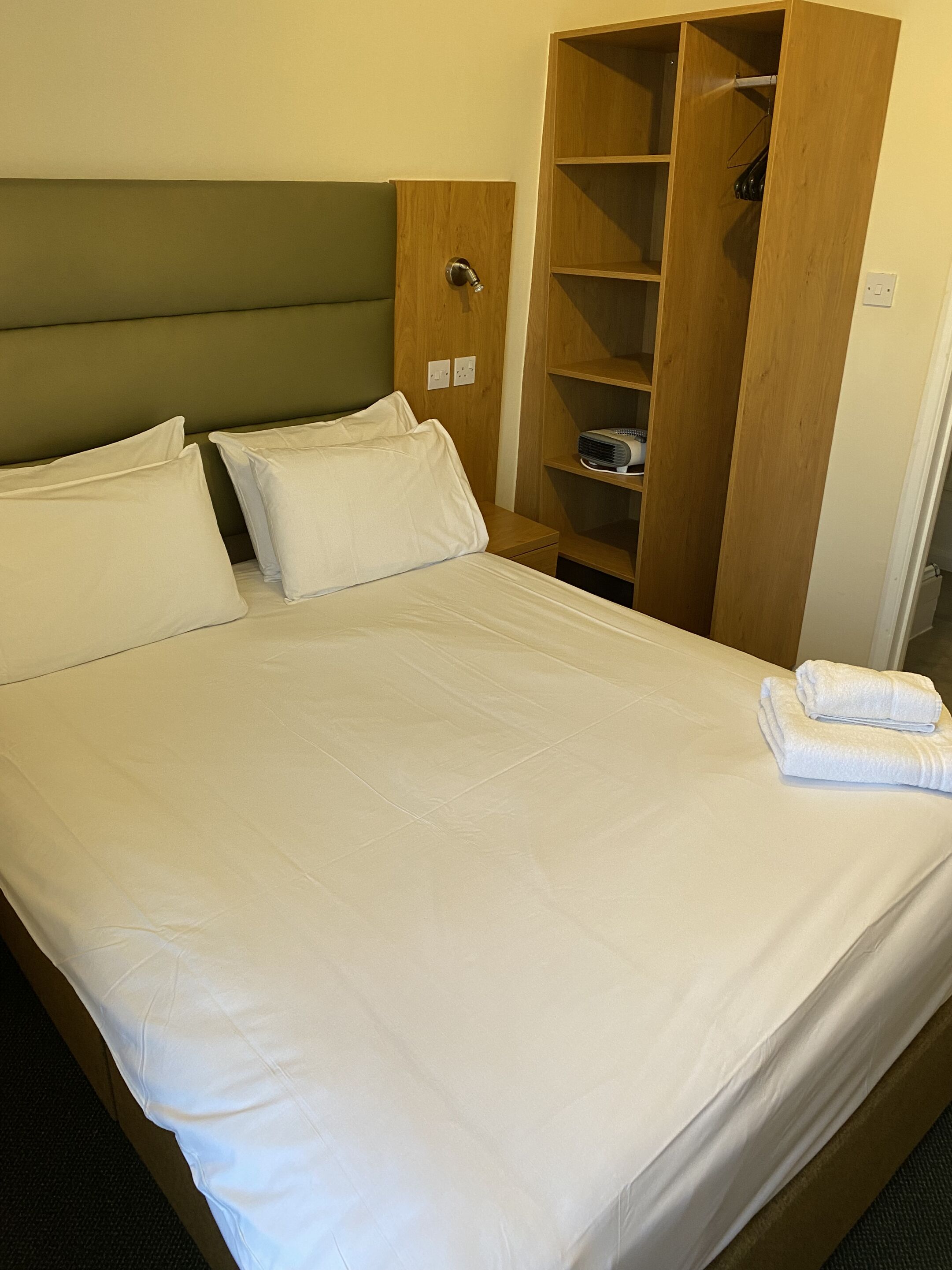 Una cama bien hecha con sábanas blancas, un cabecero de madera y un armario de madera con estantes.