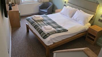 A bedroom with a large bed, a chair, a desk, and a window.