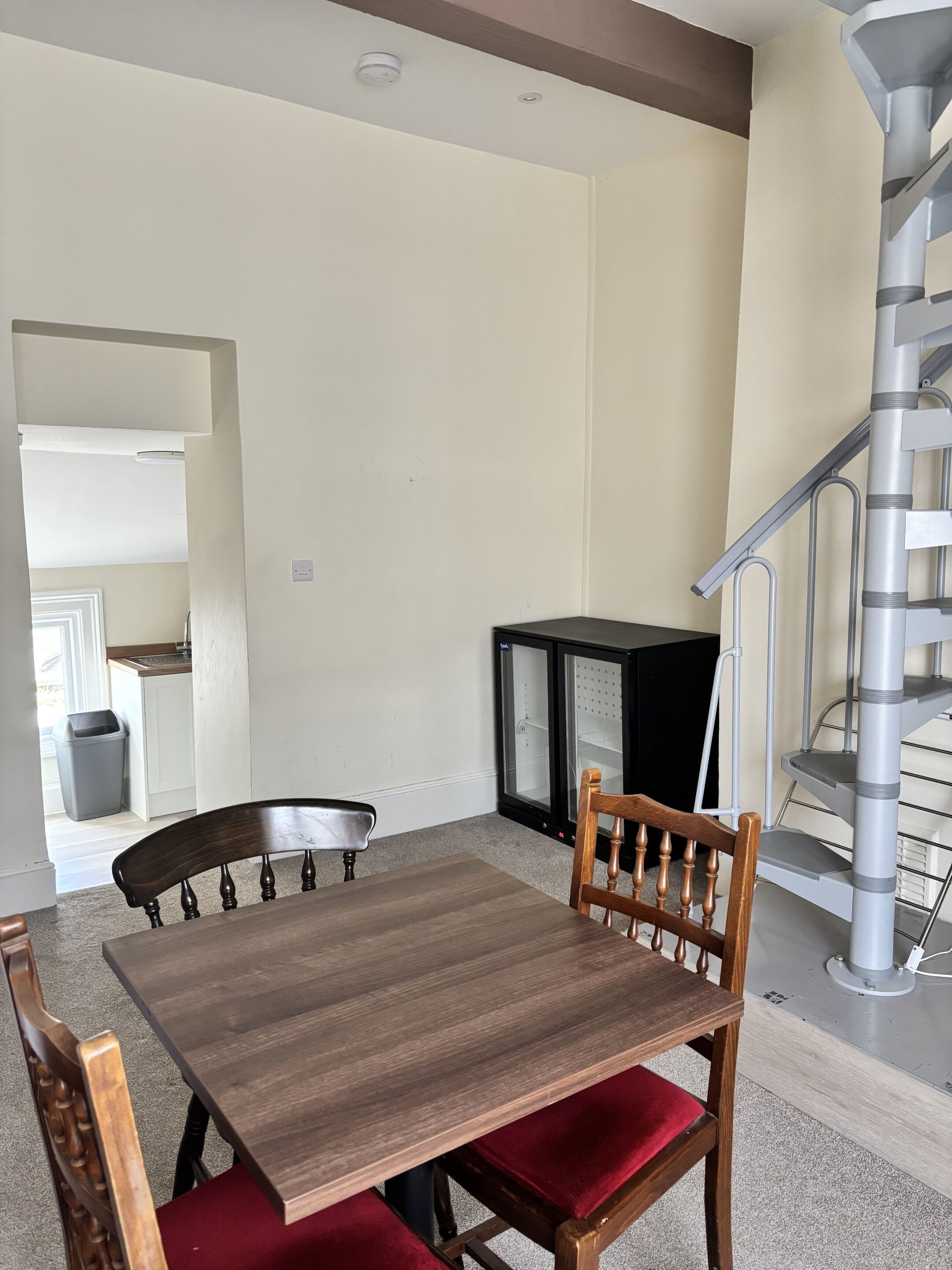 Un comedor con una mesa y sillas de madera, un refrigerador negro y una escalera en espiral.