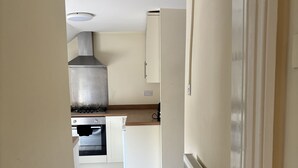 A narrow hallway leading to a kitchen with a stove, oven, and a large range hood. - The New Inn Hotel (Lechlade)