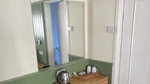 A small bathroom with a wooden vanity, a mirror, a trash bin, and a green waste bin. - The New Inn Hotel (Lechlade)