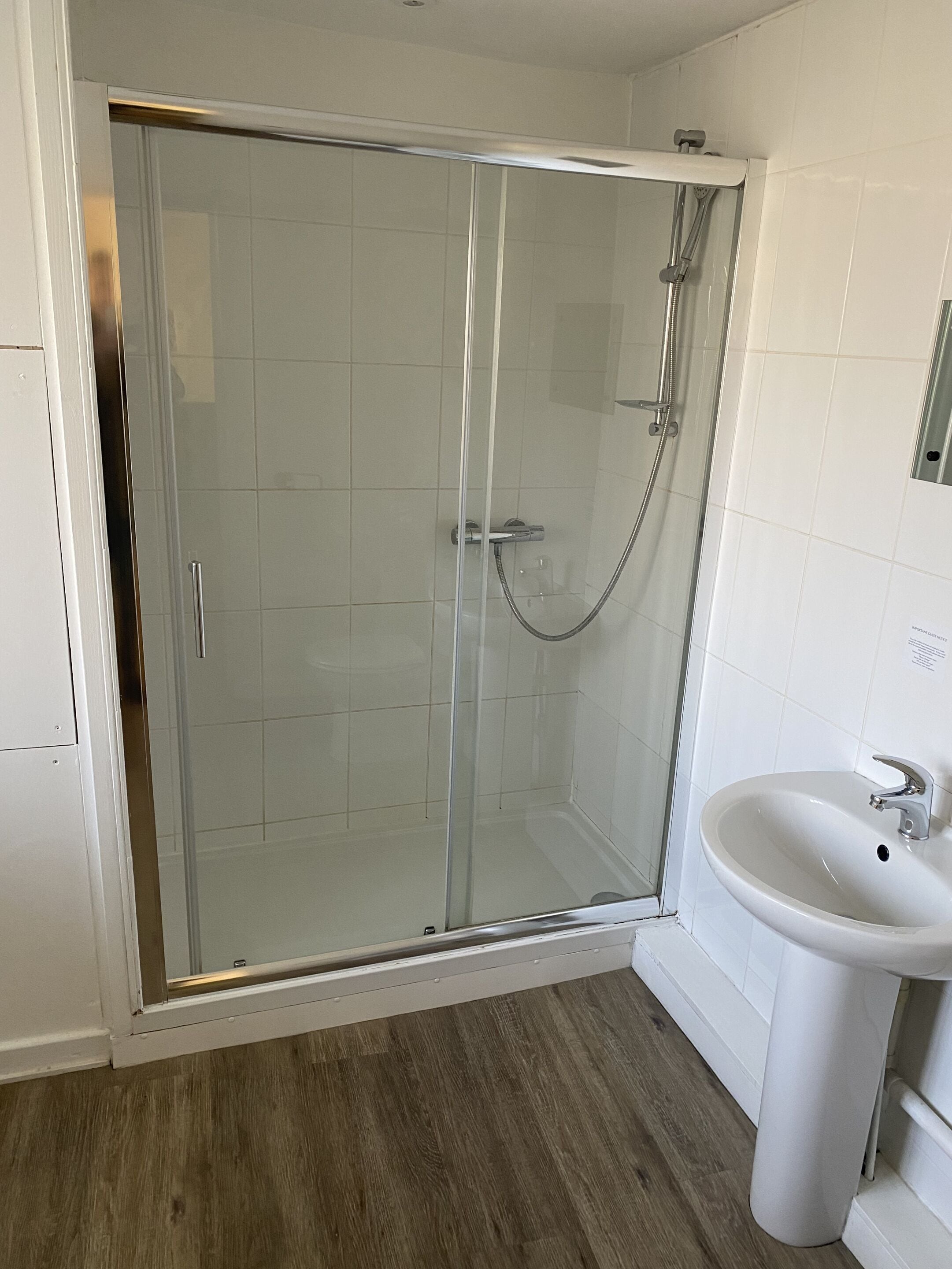 A shower with a glass door, a sink, and a wooden floor.