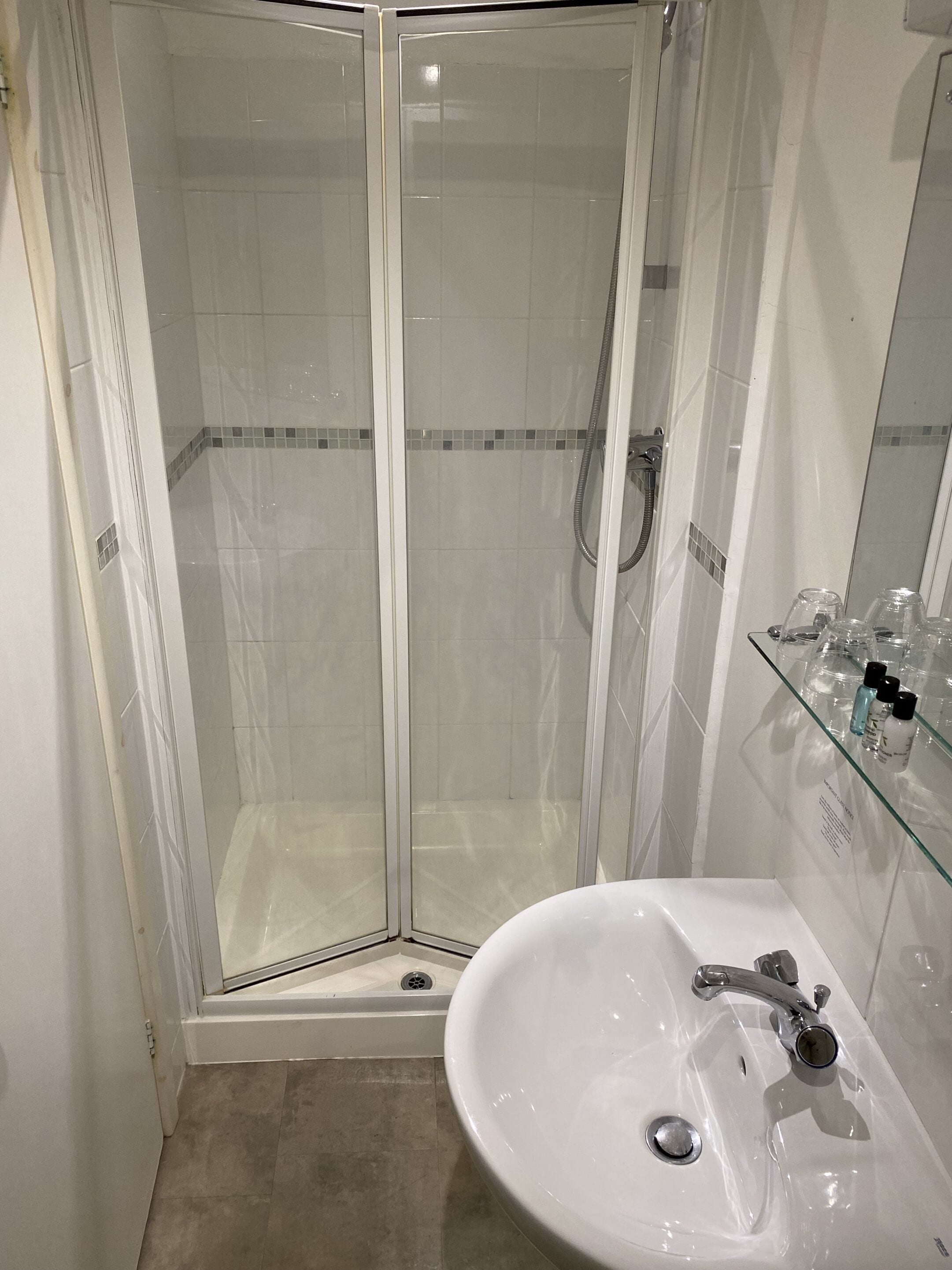 A glass-enclosed shower with a white sink and glass shelves.