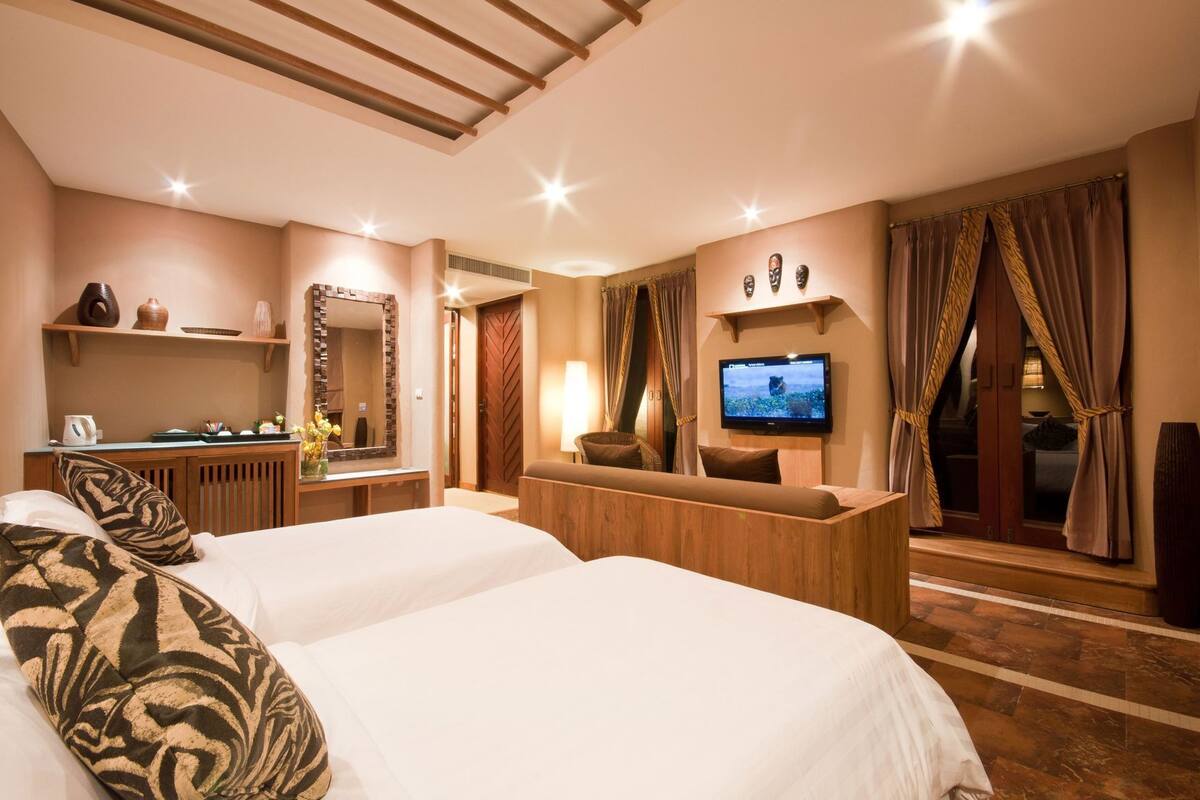 A hotel room with two beds, a TV, a desk, a mirror, and a window with curtains.