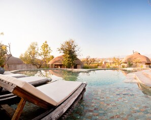 A pool area with lounge chairs, a tiled deck, and traditional thatched-roof buildings in the background. - Montis Resort (Pai)