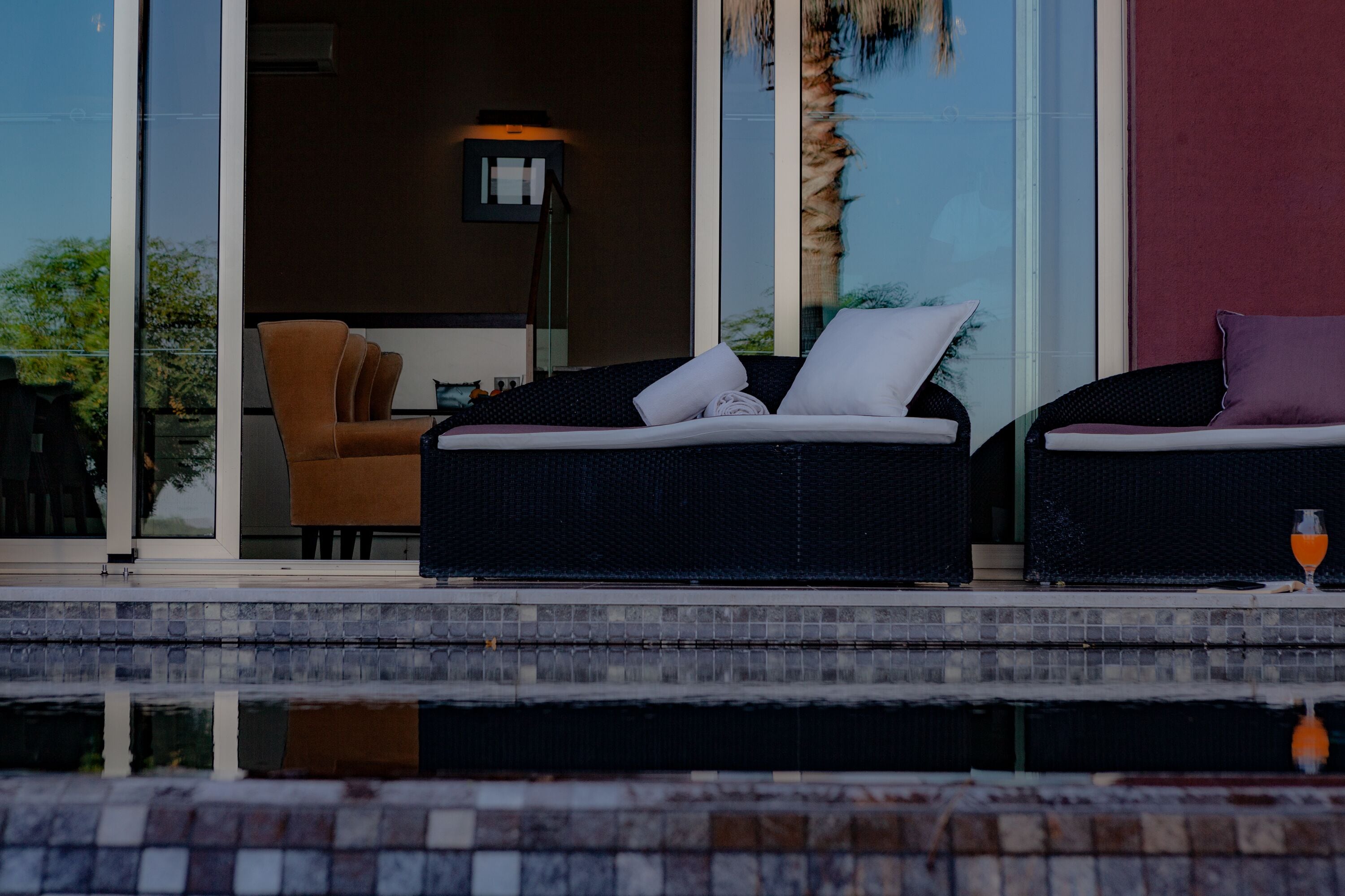 Un área de estar exterior moderna con dos sofás de mimbre y una mesa de vidrio, con vista a una piscina.