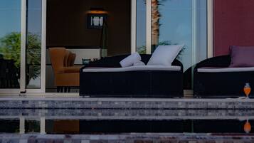 Un área de estar exterior moderna con dos sofás de mimbre y una mesa de vidrio, con vista a una piscina.