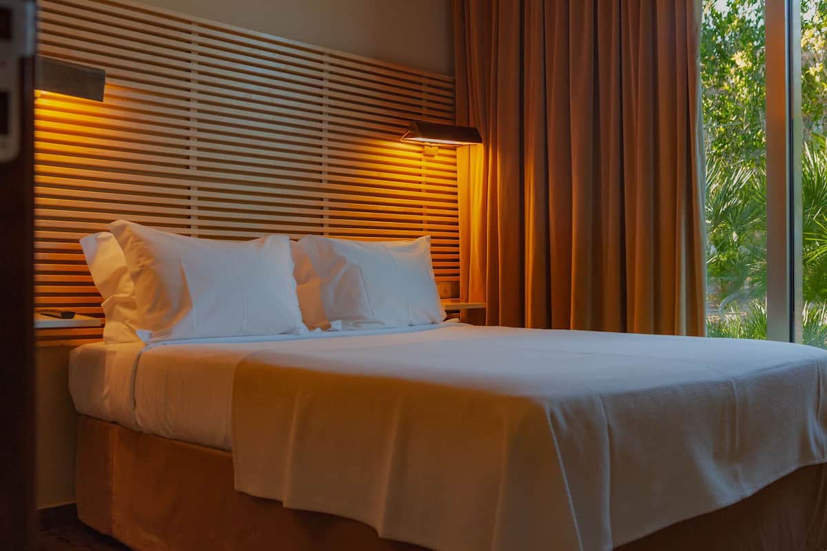 A neatly made bed with white linens and a headboard with horizontal slats.