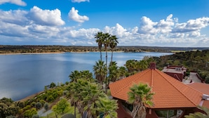 A house with a red roof, surrounded by palm trees and a lake. - Montargil Monte Novo (Ponte de Sor)