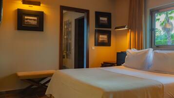 A hotel room with a bed, a bench, a small table, and framed pictures on the wall.
