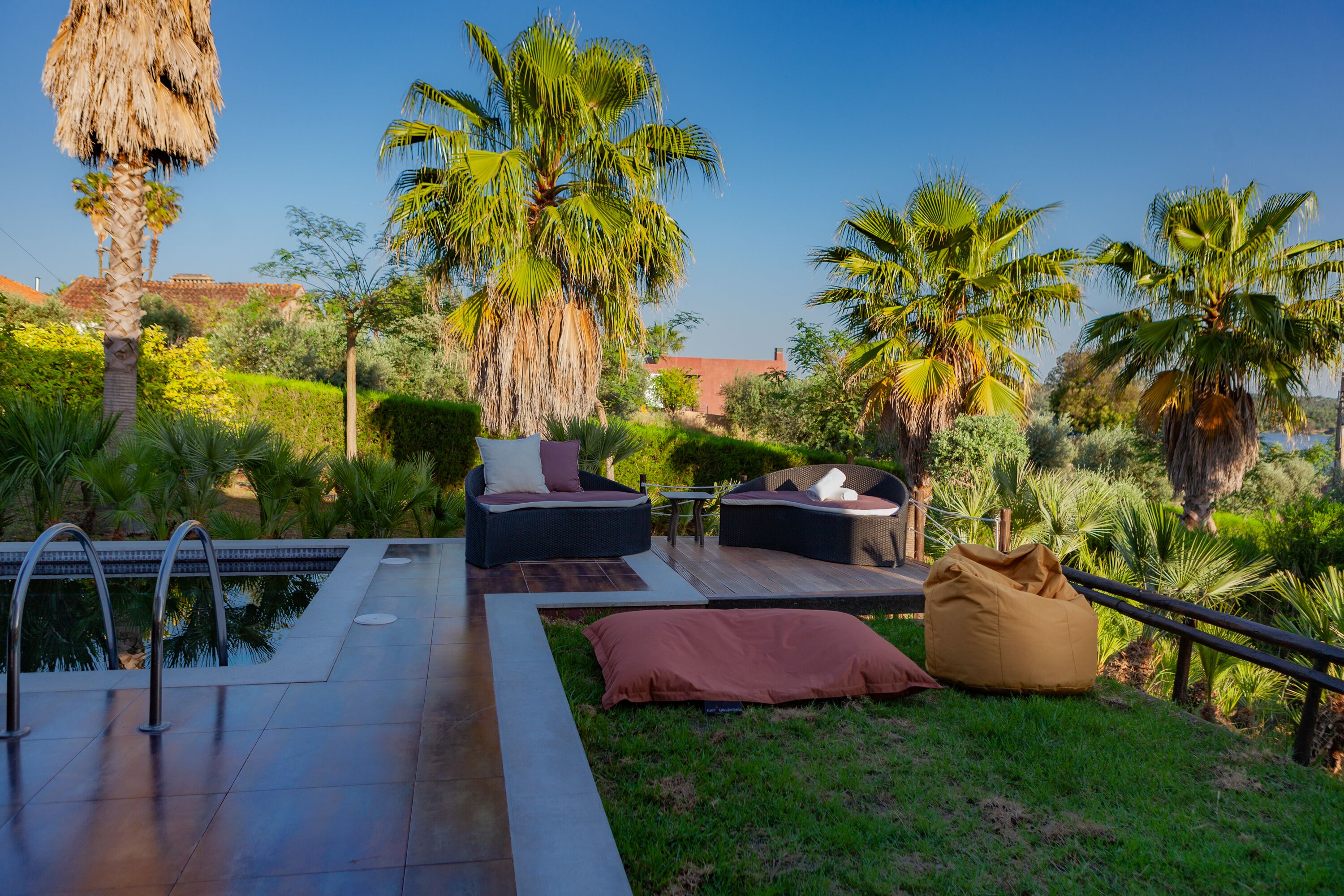 A pool area with lounge chairs and a bean bag, surrounded by palm trees and greenery.