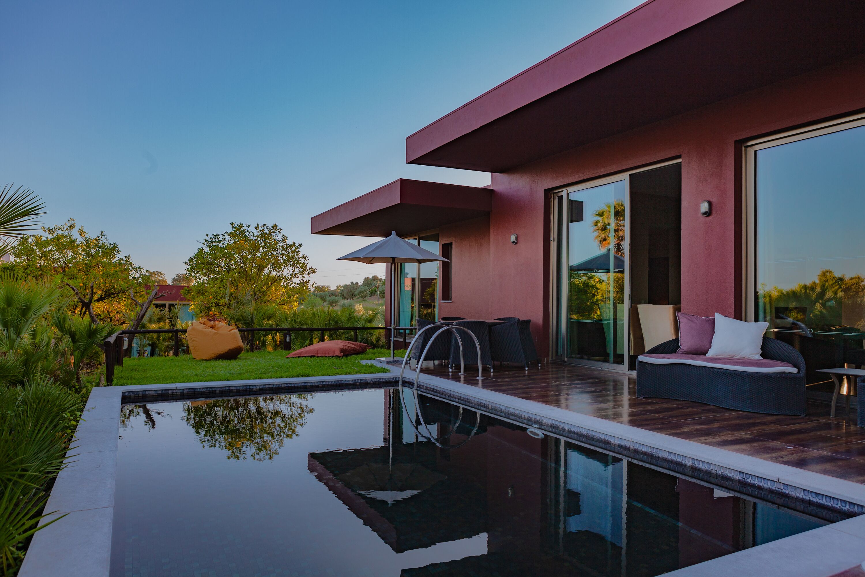 Uma área moderna com piscina ao ar livre, um lounge com paredes de vidro, um deck de madeira e uma vista clara da paisagem circundante.