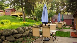 Un patio al aire libre con paredes de piedra, sillas color beige y sombrillas azules.
