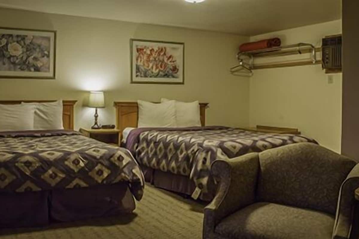 A hotel room with two beds, a chair, and a wall-mounted heater.