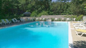 Una piscina rectangular con agua azul cristalina, rodeada de sillas de descanso blancas y una zona cubierta con una sombrilla.