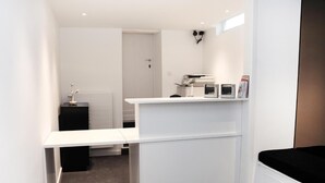 A compact, white room with a desk, a black storage unit, and a bed. - Hôtel Satellite (Brussels)