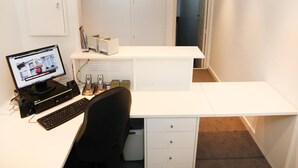 A compact office space with a desk, computer, and two mobile phones. There is a clock on the wall and a framed picture above the desk. - Hôtel Satellite (Brussels)