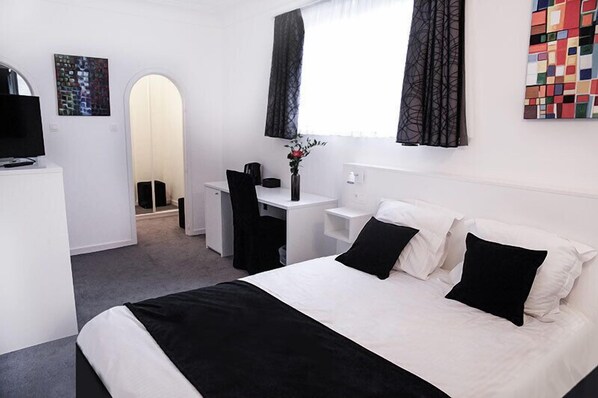 Habitación de hotel con cama, escritorio, silla, televisión y obras de arte en las paredes.