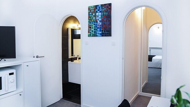 A modern hotel room with a flat-screen TV, a microwave, a bathroom with a mirror, and a colorful artwork on the wall. - Hôtel Satellite (Brussels)