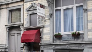 A building with a red awning, a sign indicating a hotel, and decorative window boxes with plants. - Hôtel Satellite (Brussels)