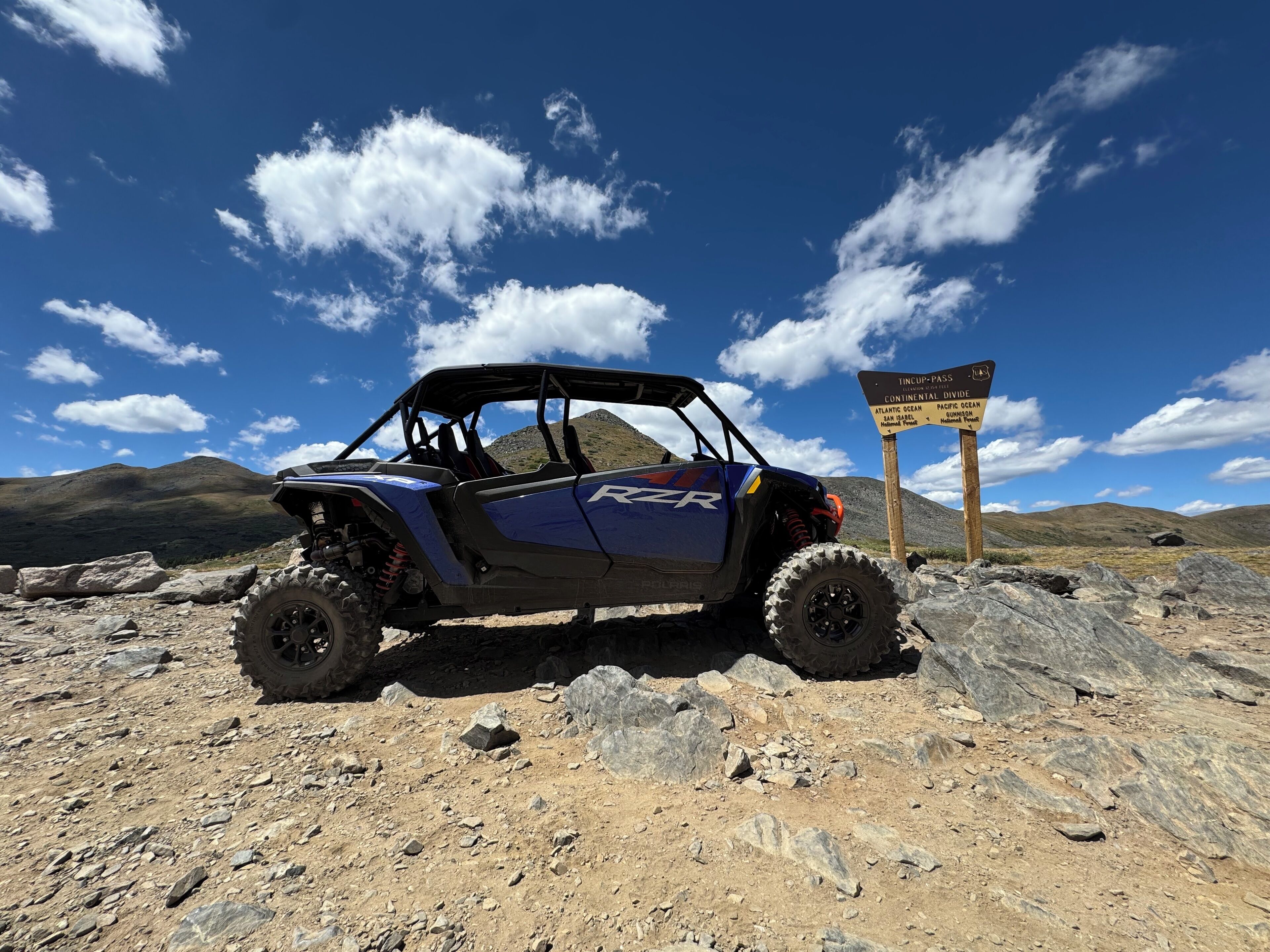 A blue off-road vehicle parked on rocky terrain with a signpost in the background.