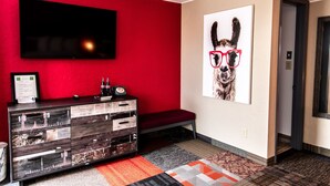 Ein modernes Wohnzimmer mit roter Akzentwand, einem flachbildfernseher, der über einem Holzkabinett angebracht ist, und einer großen Wandkunst, die einen Hund mit Brille zeigt.