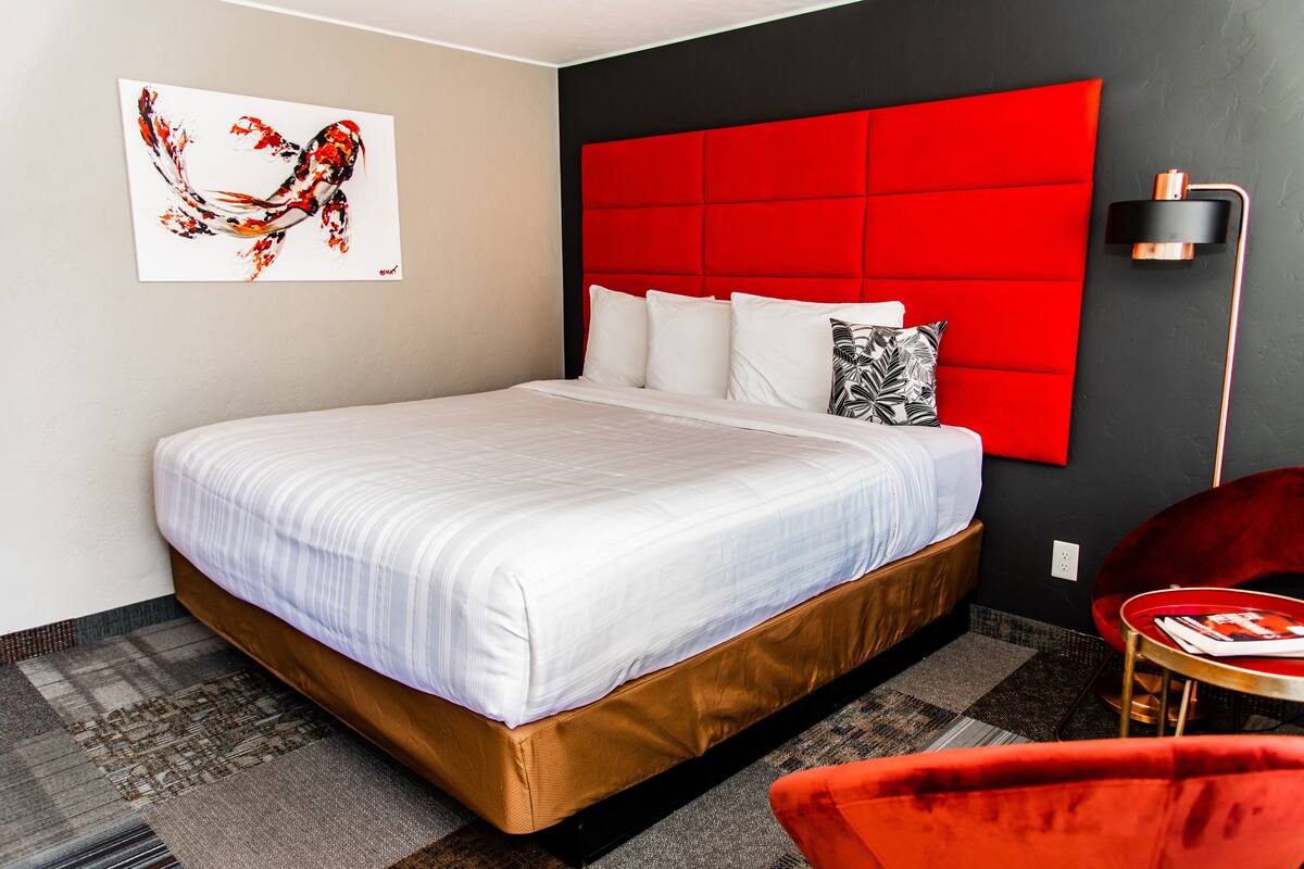 A modern hotel room with a large bed, a red headboard, and a red chair.