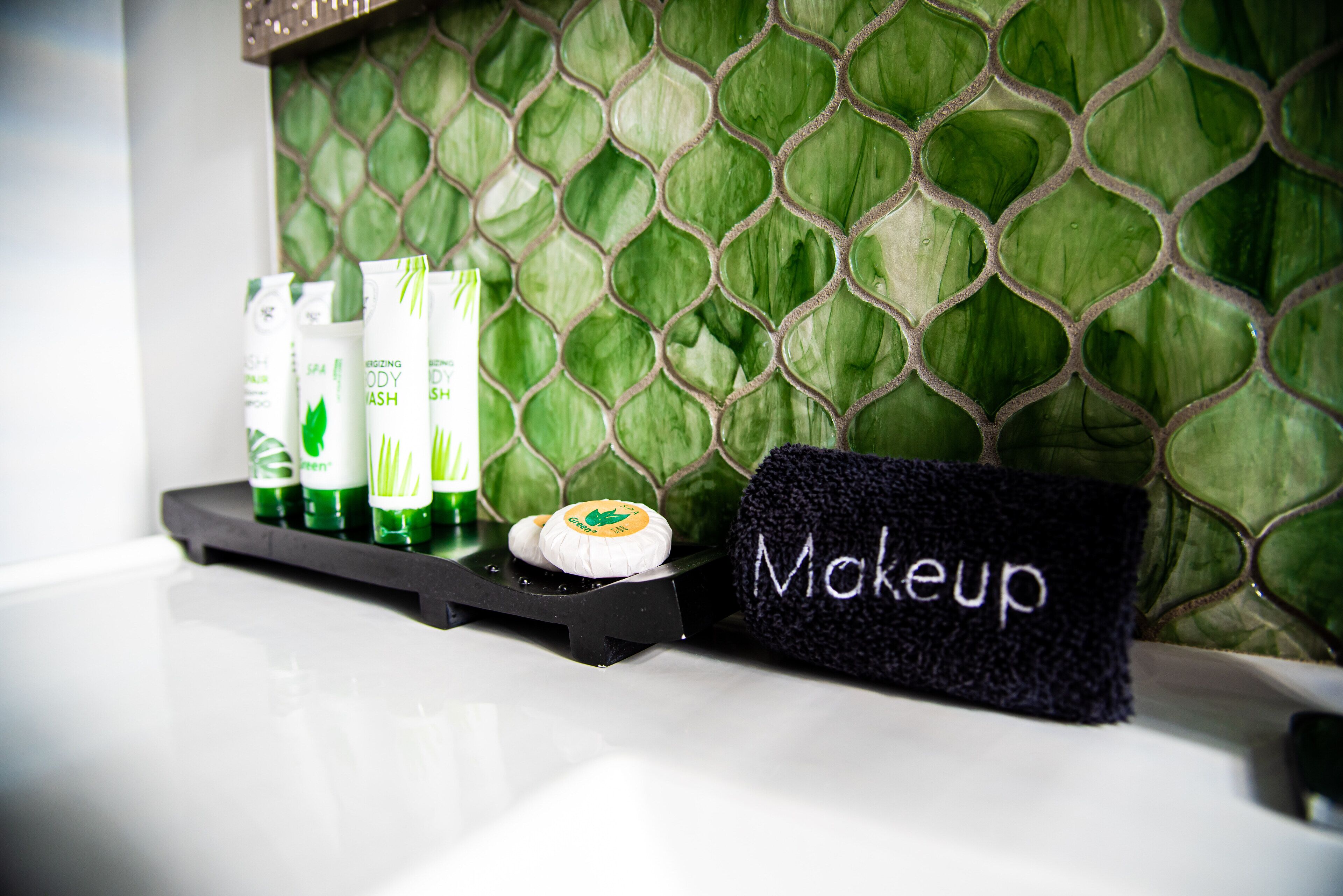 Un lavamanos de baño con un salpicadero de mosaico verde, un organizador de maquillaje y varias botellas de gel de baño y champú.