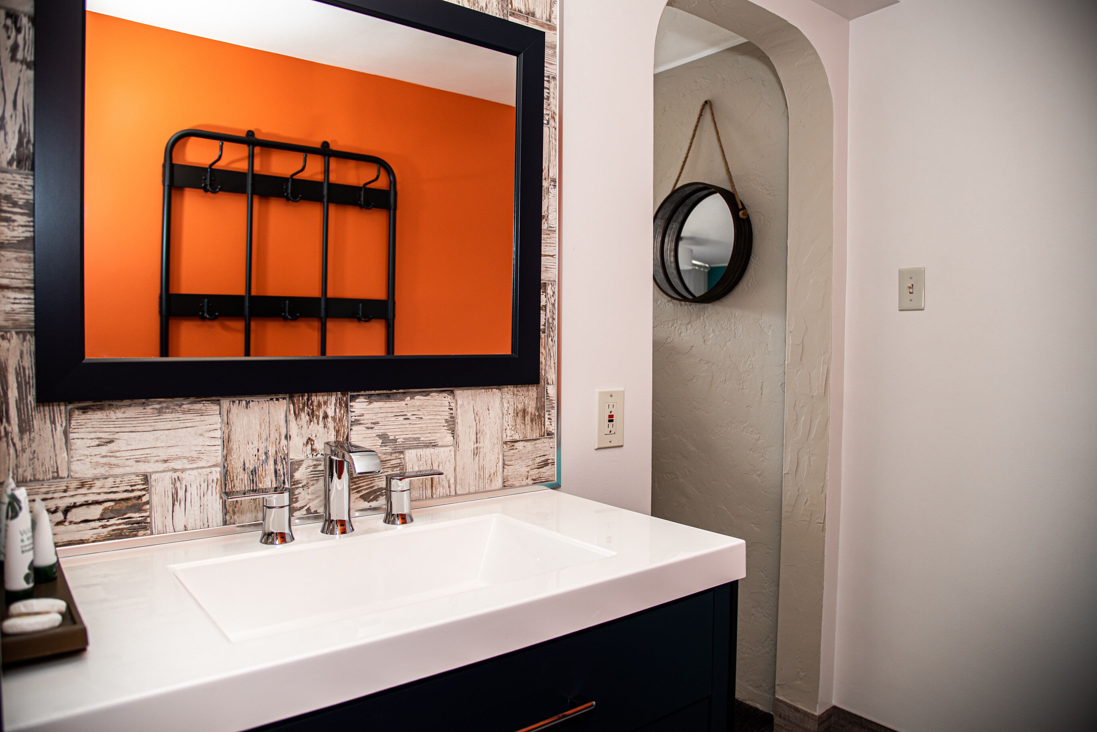 Un bagno con lavandino bianco, porta asciugamani nero e uno specchio con una parete arancione sullo sfondo.